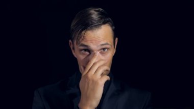 portre siyah arka plan üzerine siyah giysili bir adam. 4 k. ağır çekim. adam burnunu konturlar ve kameraya benziyor. jest yalan