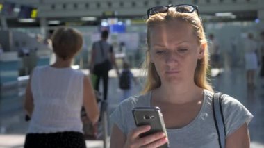 Kadın bir smartphone Havaalanı lounge bekleyen kullanır. Havaalanında uçuş beklentilerini. 4k, ağır çekim