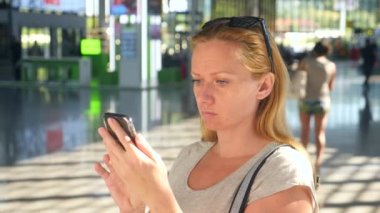 Kadın bir smartphone Havaalanı lounge bekleyen kullanır. Havaalanında uçuş beklentilerini. 4k, ağır çekim