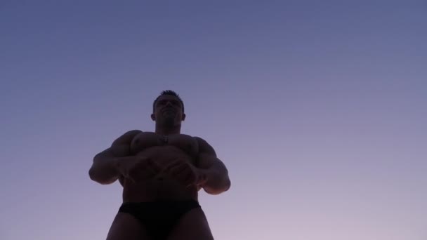 男性のボディービルダーのシルエット。夕暮れ時のビーチでポーズ美しい選手。4 k. 低速撮影 — ストック動画
