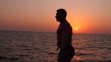 bir erkek vücut geliştirmeci silüeti. gün batımında sahilde poz güzel atlet. 4 k. yavaş çekim