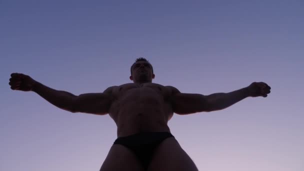 Silhouette of a male bodybuilder. beautiful athlete posing on the beach at sunset. 4k. slow shooting — Stock Video