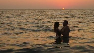 Bikini ve romantik kaslı adam hamile kadın siluetleri. vücut geliştirmeci hugs, karısını öpüyor ve karnı vuruş. Deniz günbatımı arka planı. 4 k. ağır çekim