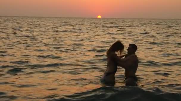 Silhouetten van zwangere vrouwen in bikini en romantische gespierde man. de bodybuilder knuffels, kussen van zijn vrouw en haar buik lijnen. tegen de achtergrond van een zonsondergang zee. 4 k. Slowmotion — Stockvideo