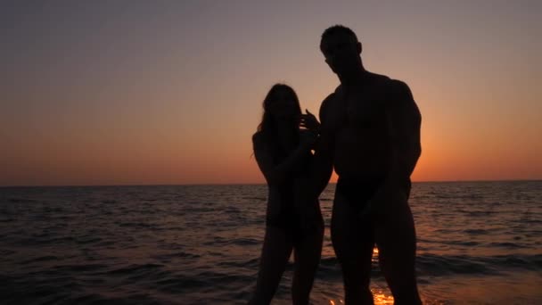 Silhuetas de mulheres grávidas em biquíni e homem musculoso romântico. o fisiculturista abraça, beija sua esposa e acaricia sua barriga. no fundo de um pôr-do-sol do mar. 4K. Movimento lento — Vídeo de Stock