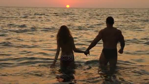 Silhouetten schwangerer Frauen im Bikini und romantischer muskulöser Mann. Der Bodybuilder umarmt, küsst seine Frau und streichelt ihren Bauch. vor dem Hintergrund eines Sonnenuntergangs am Meer. 4k. Zeitlupe — Stockvideo