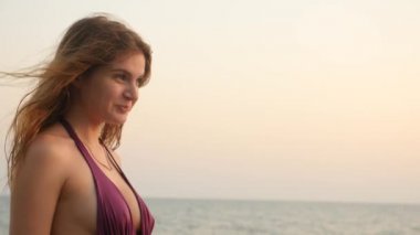 Güzel genç kız kahverengi gözleri, sevimli gülümseyen ve dalgalar deniz bir arka plan üzerinde kameraya bakıyor. 4 k yavaş hareket