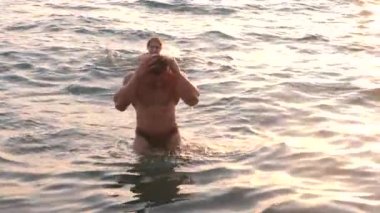 Bikini ve romantik kaslı adam hamile kadın siluetleri. vücut geliştirmeci hugs, karısını öpüyor ve karnı vuruş. Deniz günbatımı arka planı. 4 k. ağır çekim