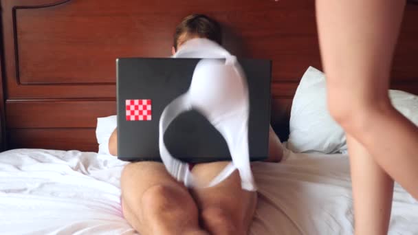 Sexy Frau versucht, Mann zu verführen, der auf Laptop im Bett arbeitet. Vor den Augen ihres Freundes zieht das Mädchen ihre Unterwäsche aus, er ignoriert sie, arbeitet an einem Laptop. 4k, Zeitlupe — Stockvideo