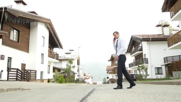Geschäftsmann vor dem Hintergrund eines Chalets, eines Hauses in den Bergen. 4k. Ein wütender Mann schwört am Telefon — Stockvideo
