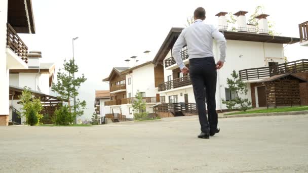 Affärsman på en bakgrund av en stuga, ett hus i fjällen. 4 k. åtnjuter syn på naturen — Stockvideo