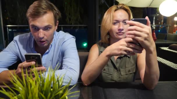 Verliebtes Paar in einem Café im Freien. Mann und schöne Frau bei einem Date. jeder schaut auf sein Handy, 4k, — Stockvideo