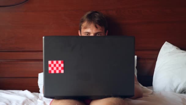 Сексуальная женщина пытается соблазнить мужчину, работающего над ноутбуком в постели. Девушка снимает нижнее белье перед своим парнем, а он игнорирует ее, работает на ноутбуке. 4k, slow motion — стоковое видео