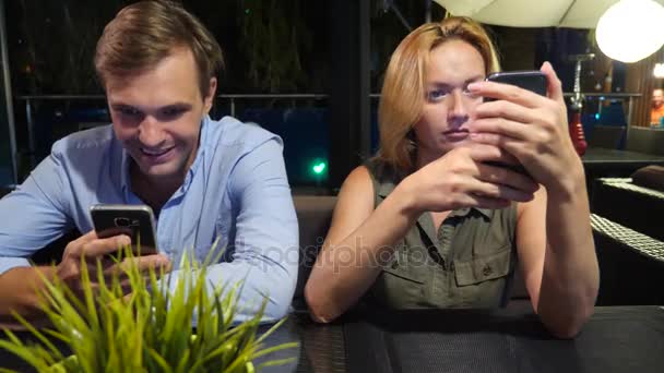 Pareja enamorada en un café al aire libre. Hombre y mujer hermosa en una cita. Todo el mundo está mirando su teléfono móvil, 4k , — Vídeo de stock