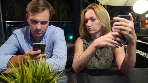 Paar verliefd op een terras. Man en mooie vrouw op een datum. Iedereen is op zoek op zijn mobiele telefoon, 4k, — Stockvideo