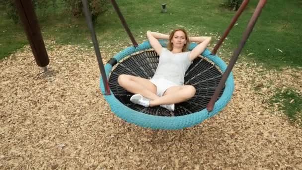 Jeune femme balançant sur une balançoire un hamac sur le parc d'attractions de la ville. 4k, espace de copie — Video