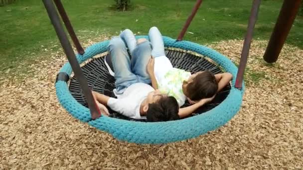 Chico y chica, gemelos balanceándose en un columpio una hamaca en el parque de atracciones de la ciudad. 4k, espacio de copia — Vídeos de Stock