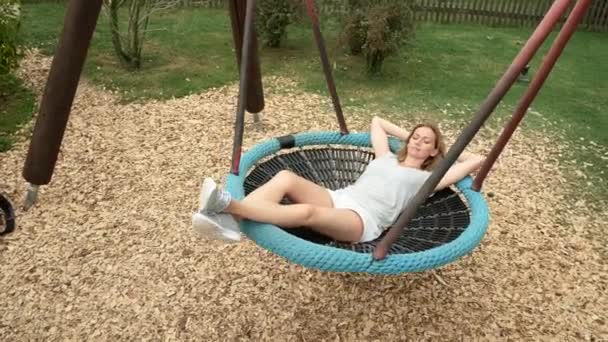 Joven mujer balanceándose en un columpio una hamaca en el parque de atracciones de la ciudad. 4k, espacio de copia — Vídeos de Stock