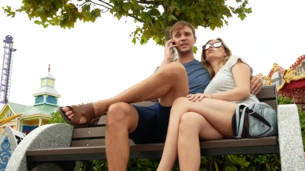 Joyeux famille assis sur un banc dans un parc d'attractions et amusez-vous. 4k. espace de copie. style de vie — Video