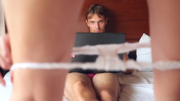 Donna sexy che cerca di sedurre l'uomo che lavora sul computer portatile a letto. la ragazza si toglie le mutande davanti al suo ragazzo, e lui la ignora, lavora su un computer portatile. 4k, rallentatore — Video Stock