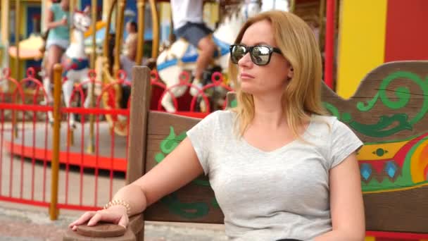 Счастливая женщина, сидящая на скамейке в парке развлечений. 4k Медленное движение. скопировать пространство. стиль жизни, парк Сочи, сентябрь 2017 — стоковое видео