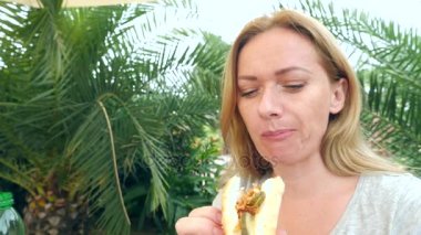 Çekici bir kız taze pide ekmek taze sebze ve et, parkta bir ağacın altında bir lokanta kafede oturan salata yiyor. 4 k yavaş hareket
