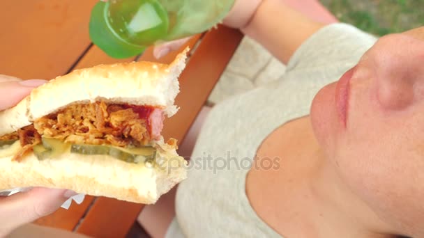 Egy vonzó lány eszik friss pita kenyér, a saláta, friss zöldségek és a hús, ül a parkban egy fa alatt egy gyorsétterem kávézóban. 4 k-lassú mozgás — Stock videók