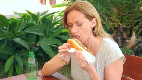 Een aantrekkelijk meisje eet vers pita brood met een salade van verse groenten en vlees, zitten in een cafe fastfood onder een boom in het park. 4 k slow-motion — Stockvideo