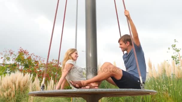 Pareja romántica joven mujer y hombre balanceándose en un columpio en el parque de atracciones de la ciudad. 4k, copia el espacio. Movimiento lento — Vídeos de Stock