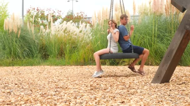 Romantische koppel jonge vrouw en man swingen op een schommel op het attractiepark in de stad. 4k, kopie ruimte. Slow motion — Stockvideo