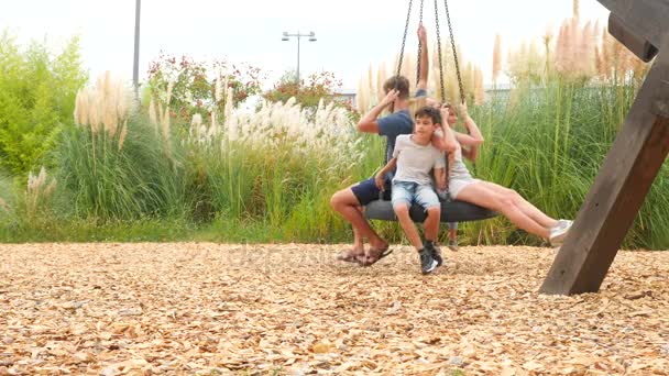 Gelukkige familie moeder, vader, zoon en dochter swingende op een schommel op het attractiepark in de stad. 4k, kopie ruimte. Slow-motion. Privaatleven. — Stockvideo