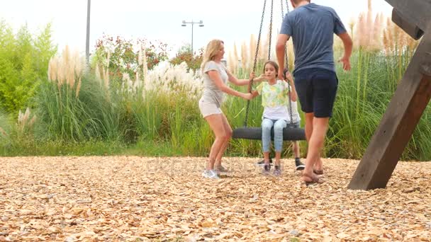Familia feliz mamá, papá, hijo e hija balanceándose en un columpio en el parque de atracciones de la ciudad. 4k, copia el espacio. En cámara lenta. estilo de vida . — Vídeo de stock