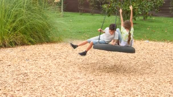 Irmão feliz e irmã balançando em um balanço no parque de diversões na cidade. 4K, espaço de cópia, câmera lenta. estilo de vida — Vídeo de Stock