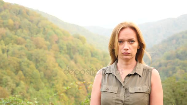 Крупный план портрета красивой молодой женщины с светлыми волосами, дующими на ветру и смотрящими на гору. Slow Motion 4k — стоковое видео