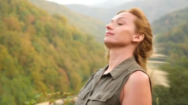 Primer plano retrato de una hermosa joven con el pelo rubio soplando en el viento mirando a la montaña. Moción lenta 4k — Vídeo de stock