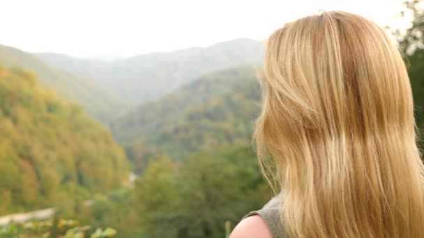 Primer plano retrato de una hermosa joven con el pelo rubio soplando en el viento mirando a la montaña. Moción lenta 4k — Vídeos de Stock