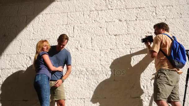 Casal adulto alegre posando para um fotógrafo profissional contra um fundo de parede de tijolo branco. 4k, câmera lenta, espaço de cópia — Vídeo de Stock