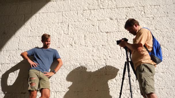 Неслухняний хлопець, створюючи для професійного фотографа на стіні з білої цегли. 4k, повільний рух, простір копіювання — стокове відео