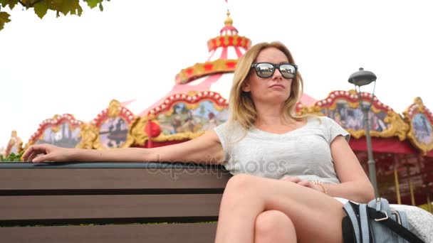 Lycklig kvinna sitter på en bänk i en nöjespark. 4 k slowmotion. Kopiera utrymme. livsstil, Sochi Park, September 2017 — Stockvideo