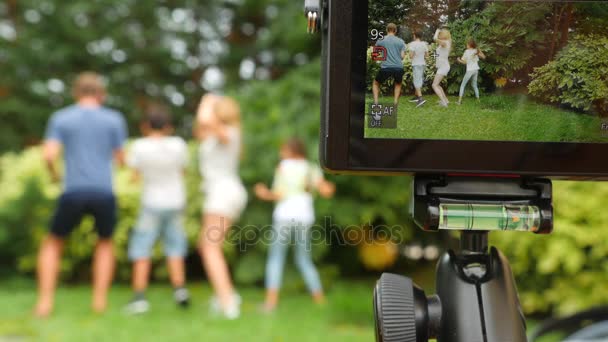 Записать семейное видео на видеокамеру. Счастливая семья танцует вместе на траве в парке с красивой природой. 4k. скопировать пространство. стиль жизни. Медленное движение — стоковое видео