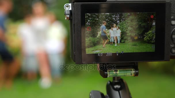 Gravar vídeo da família em sua filmadora. Família feliz dançando juntos na grama em um parque com bela natureza. 4K. espaço de cópia. estilo de vida. Movimento lento — Vídeo de Stock