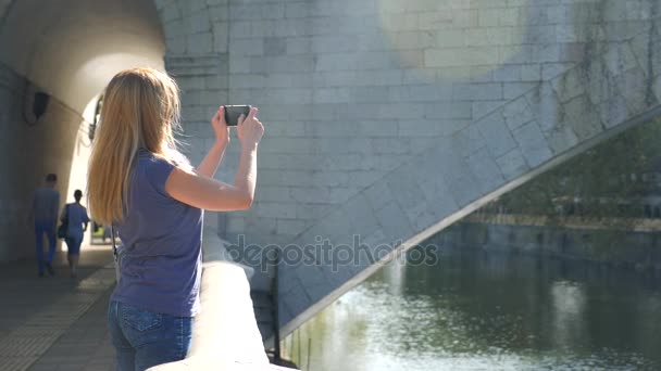 Hermosa mujer adulta joven tomando fotos de sí misma, selfie. contra el fondo del puente sobre el río. 4k, grabación en cámara lenta, espacio para copiar . — Vídeos de Stock