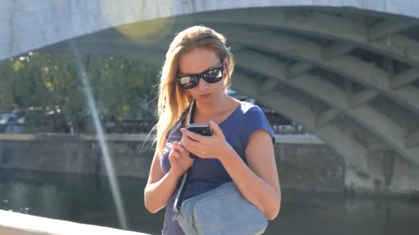 大人の美しい若い女性彼女自身は、selfie の写真を撮る。川に架かる橋を背景。4 k、スローモーション撮影、コピー スペース. — ストック動画
