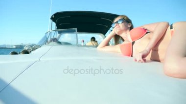 Çekici kadın denizde bir yaz gününde bir yatta. ince busty sarışın uzun saçlı, güneş gözlüğü ve parlak kırmızı bikini giyen açık denizde bir teknenin güvertesinde güneşlenirken.