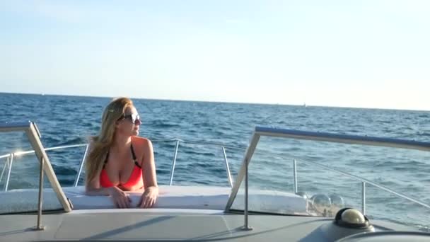 Attraktive Frau auf einer Jacht an einem Sommertag auf See. Die schlanke, vollbusige Blondine mit langen Haaren, Sonnenbrille und knallrotem Bikini sonnt sich an Deck eines Bootes auf hoher See. 4 , — Stockvideo