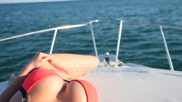 Donna attraente su uno yacht in una giornata estiva in mare. sottile procace bionda con i capelli lunghi, indossa occhiali da sole e un bikini rosso brillante sta prendendo il sole sul ponte di una barca in mare aperto . — Video Stock