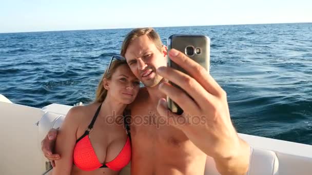 Счастливая любящая пара, сидящая вместе на яхте, делая селфи на своем смартфоне. 4k, slow motion — стоковое видео