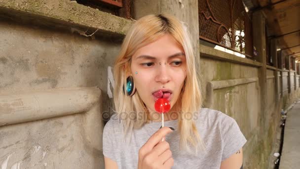 Mitificação corporal. Uma rapariga com a língua partida lambe chupa-chupa. 4k, tiro em câmera lenta, espaço de cópia — Vídeo de Stock