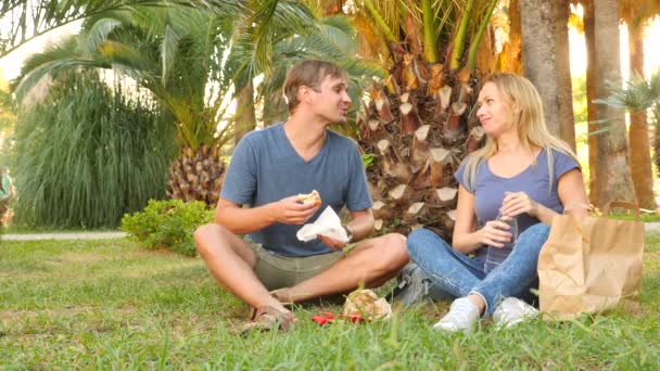 Um casal feliz a comer hambúrgueres. Ao ar livre. lanche fast food. 4k, câmera lenta — Vídeo de Stock