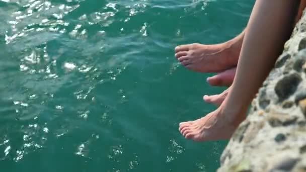 Una pareja sentada en el muelle y moja los pies en el mar. 4k, cámara lenta — Vídeos de Stock